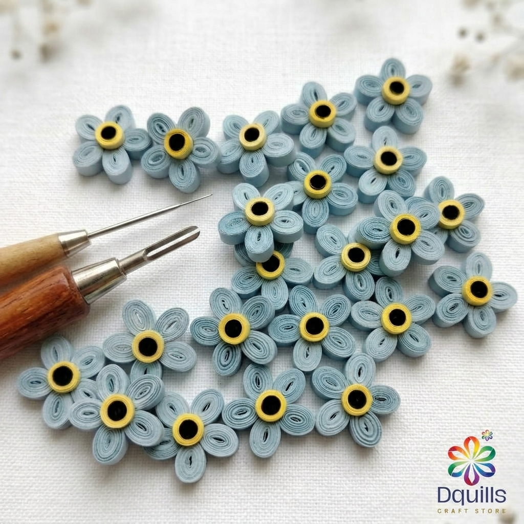Close-up of soft blue handmade quilled forget-me-not flowers arranged on a white surface with a quilling tool by Dquills